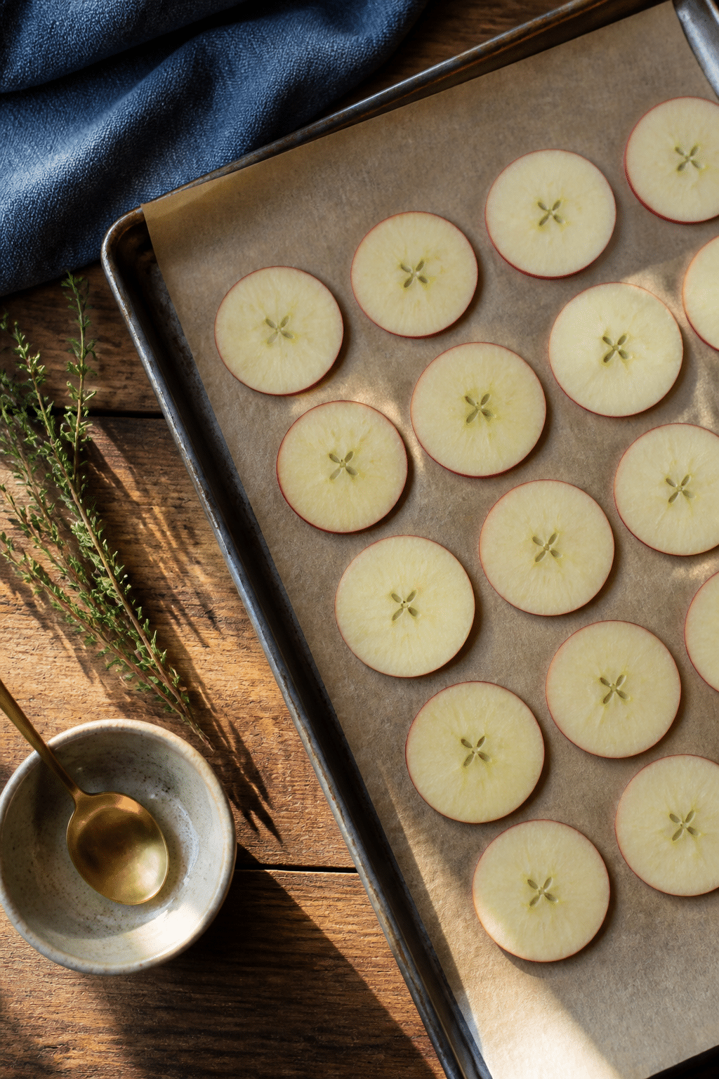 Thin apple slices arranged on a parchment-lined baking sheet